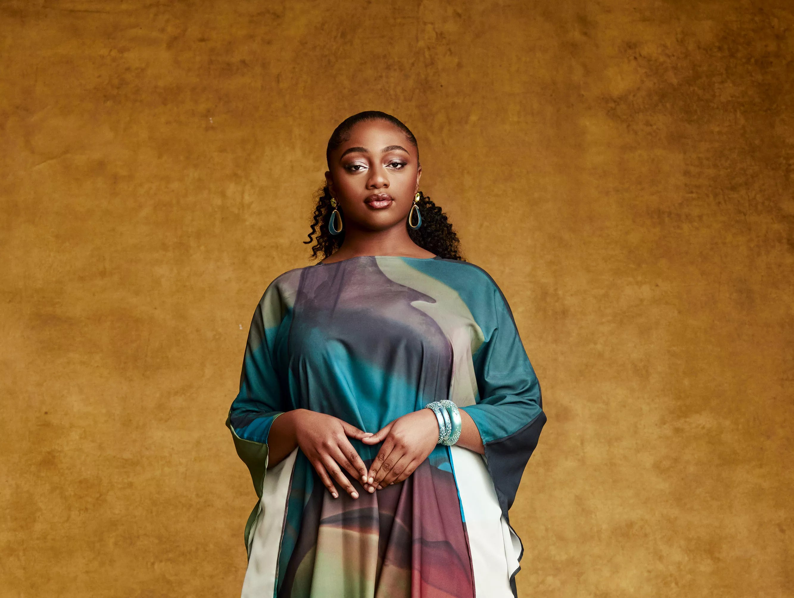A woman standing in front of orange background.